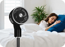 A black TCP standing fan and a woman sleeping behind it